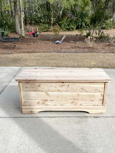 a wooden box sitting on top of a cement ground next to trees and bushes in the background