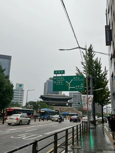 cars are driving down the street in front of tall buildings on a rainy day with green and white signs