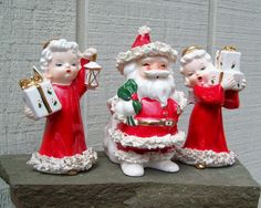 three santa figurines are standing on a ledge with presents in their hands and one is holding a present