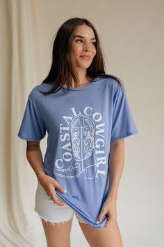 Introducing our Coastal Cowgirl Light Blue Graphic Tee, where western charm meets coastal cool for an effortlessly chic look. Crafted from soft and breathable light blue fabric, this tee offers both style and comfort for any occasion. At the heart of its design is a striking white cowgirl boot graphic, capturing the essence of western spirit and adventure. Wrapped around the boot, the "Coastal Cowgirl" text in crisp white adds a touch of seaside flair, blending rugged charm with laid-back coasta Washed Blue Graphic Tee With Print, Washed Blue Graphic Tee With Graphic Print, Summer Washed Blue Tops With Graphic Print, Summer Washed Blue Graphic Print Tops, Washed Blue Graphic Print Short Sleeve Top, Short Sleeve Washed Blue Top With Graphic Print, Washed Blue Relaxed Fit Graphic Top, Relaxed Fit Washed Blue Graphic Print Top, Light Wash Graphic Tee With Crew Neck