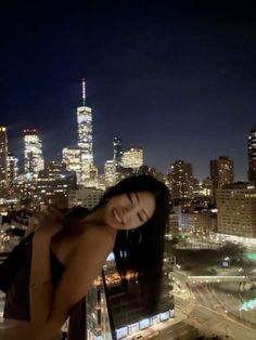 a woman standing on top of a building in front of a cityscape at night