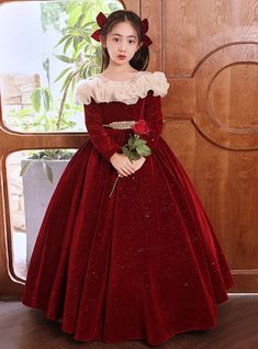 Bathed in the rich hues of royal elegance, our red velvet flower girl dress is the epitome of timeless beauty. The sumptuous velvet fabric offers a luxurious feel, while the soft ivory ruffled neckline adds a touch of classic sophistication. The long sleeves provide a warm and elegant look, ideal for formal occasions. A shimmering golden belt at the waist enhances the silhouette, leading to a full, glittering skirt that twinkles with every movement. This dress is designed to ensure your flower girl feels comfortable and looks stunning, no matter the celebration. Perfect for guiding the bride down the aisle or dancing joyfully at the reception, this gown guarantees she will radiate charm and grace. Make her feel like royalty with this exquisite dress, thoughtfully crafted to make your speci Bride Down The Aisle, Burgundy Flower Girl Dress, Golden Belt, Sleeveless Flower Girl Dresses, Purple Tulle, Velvet Flower, Glitters Skirt, Velvet Flowers, Quinceanera Dress