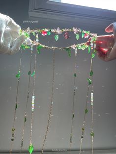 two hands are holding some green and pink beads with chains attached to the sides, while another hand holds something in front of them