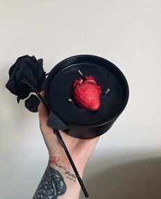 a person holding a black bowl with a red heart in it and a rose on the side