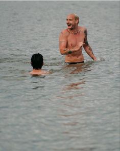 a man standing in the water with his arm around another man's waist, both looking at each other