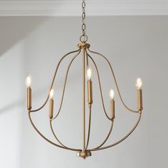 a chandelier with five lit candles hanging from it's center, in a white room