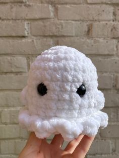 a hand holding up a small white crocheted object with black eyes on it