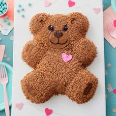 a brown teddy bear cake sitting on top of a white plate next to pink and blue plates