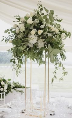 a tall vase filled with white flowers and greenery sitting on top of a table