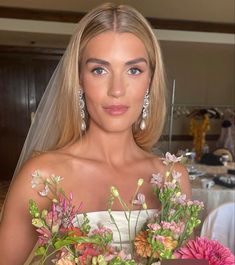 a woman wearing a wedding dress holding flowers in her hand and looking at the camera