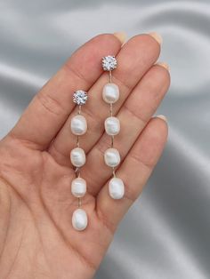 a woman's hand holding three white pearls and a diamond earring on top of it