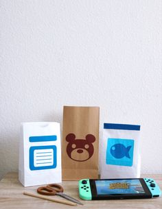 some paper bags are sitting on a table next to scissors and a cell phone with a bear face drawn on it