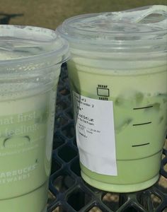 two plastic cups sitting on top of a metal table next to each other with green liquid in them