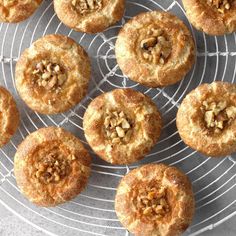 many small pastries are on a wire rack with some nuts in the top one