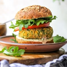 a burger with lettuce, tomato and cheese on a plate next to a bowl