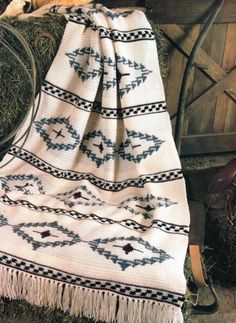 a white blanket with black and grey designs on it sitting next to a wooden chair