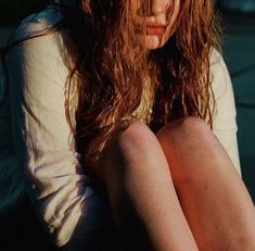 a young woman sitting on the ground with her legs crossed and hair blowing in the wind