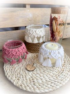 three knitted candle holders sitting on top of a wicker tray next to a vase