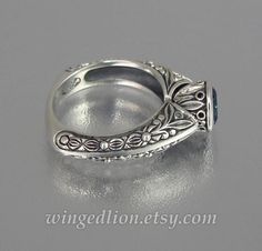 a silver ring with filigrees and scrolls on the sides, sitting on a gray surface