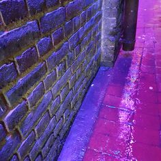 a brick wall next to a sidewalk with purple paint on it and a fire hydrant in the background