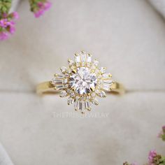 a diamond ring sitting on top of a white box with flowers in the back ground