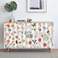 a white cabinet with flowers on it next to a potted plant and framed photograph