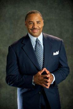 a man in a suit and tie posing for a photo with his hands folded on his chest