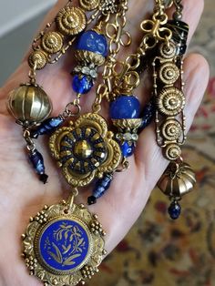 An assemblage with a Victorian sensibility. The central pendant is a vintage Czech glass button mounted in a brass French quatrefoil shape with a French lion button on the back. It suspends a Freirich brooch from the 1950s. It is gold plated with a botanical floral center and navy blue enamel. I've removed the pin back so it lays flat. On either side are vintage brass findings holding vintage Ethnic beads from Sri Lanka terminating in vintage glass beads of West German origin. Other pendants are vintage brass and rhinestone caps, vintage Japanese dimple glass, and vintage lampwork from India. I've used large gold plated links and a brass hook so length can be adjusted. Vintage Brass Brooch Jewelry, Fashion Nonbinary, Artistic Accessories, Designing Jewelry, Altered Art Jewelry, Found Object Jewelry, Vintage Jewelry Ideas, Lamp Makeover, Edith Piaf