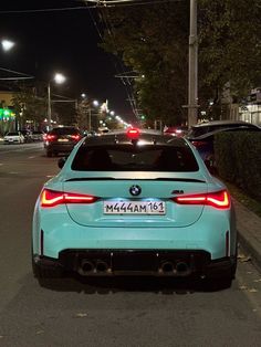 a blue bmw car parked on the side of the road at night with its lights on