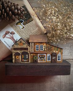 a small wooden house sitting on top of a table next to a book and pine cone