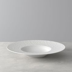 an empty white bowl sitting on top of a gray tableclothed floor with a grey wall in the background