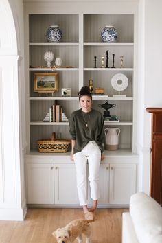 a woman sitting on top of a white book shelf next to a brown and white dog