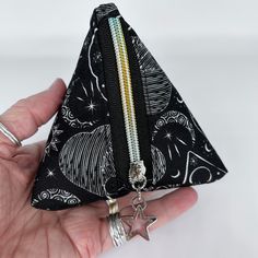 a hand holding a small triangle shaped pouch with two zippers on each side and a star charm hanging from the bottom