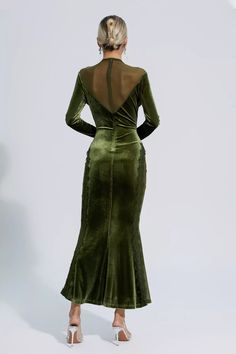 a woman wearing a green velvet dress with sheer shoulders and back cut out, standing in front of a white background