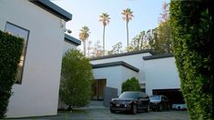 two cars parked in front of a white house with palm trees on the other side