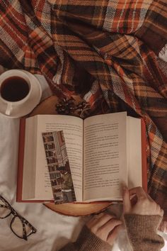 a person reading a book on top of a bed next to a cup of coffee