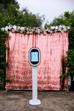 an electronic device is standing in front of a pink backdrop with white flowers on it