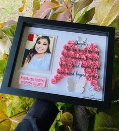 a person holding up a framed photo with pink flowers in the shape of a heart