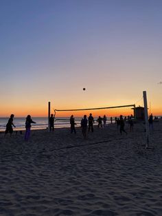 people playing volleyball on the beach at sunset