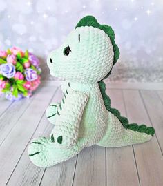 a crocheted stuffed alligator sits on a wooden floor next to flowers and a bouquet