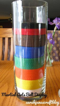 a glass filled with lots of different colored ribbons on top of a wooden table next to a vase