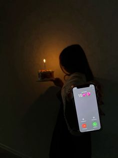 a person holding a cell phone in their hand with a lit candle on the wall behind them