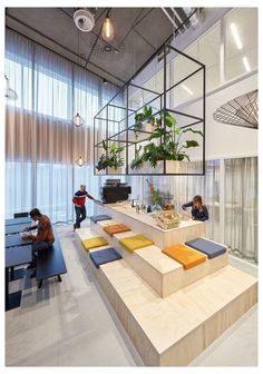 people are sitting at tables in an office with plants on the desks and shelves