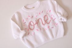 Beautiful hand embroidered ONE chunky sweater. Perfect for your baby's first birthday.  This listing is for one sweater only. You pick the wording from 1/2, ONE, or TWO White Sweater and pink lettering plus sprinkles as pictured. If you want a different color, just send us a convo. We'll be happy to customize for you Hand embroidery on a chunky sweater True to size Custom orders welcome Cute White Sweater With Embroidered Text, White Cute Sweater With Embroidered Text, Cute Crew Neck Birthday Sweater, Cute Crew Neck Sweater For Birthday, Cute Sweater For Birthday In Winter, Cute Cotton Sweater For Birthday, Embroidered Winter Birthday Sweater, Cotton Crew Neck Sweater For Birthday, Hand Embroidered Sweater