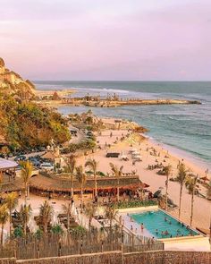 an aerial view of the beach and pool area at sunset, with palm trees in the foreground