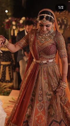 a woman in a red and gold bridal gown is holding the hand of her groom