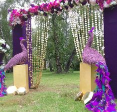 two purple peacocks are standing in front of an arch decorated with flowers and feathers