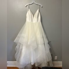 a white dress hanging on a hanger in front of a gray wall and wooden floor