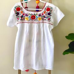 a white blouse with colorful flowers and tassels hanging on a clothes hanger