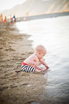 a baby playing in the sand on the beach with his feet in the ocean water